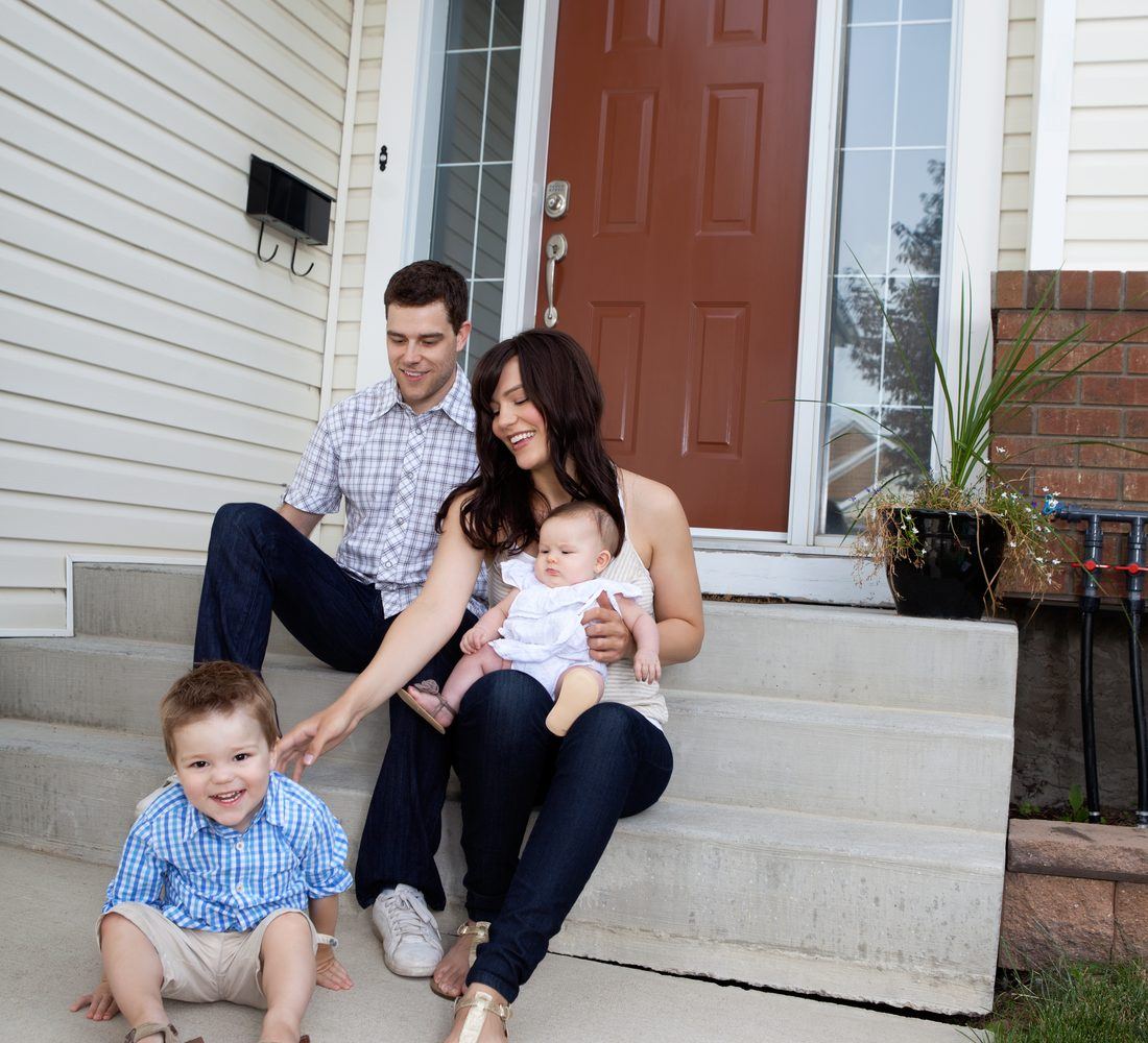 Parents and two young children sitting on the front steps of their home