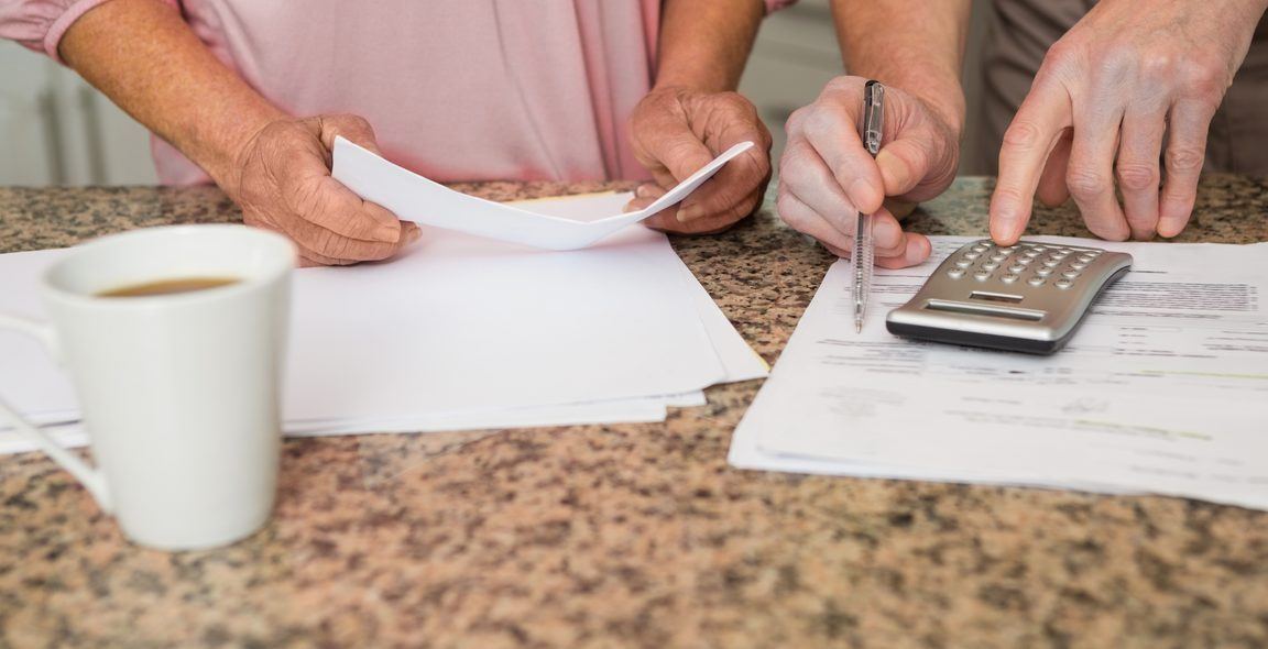 Two people going through statements and a calculator at a kitchen counter